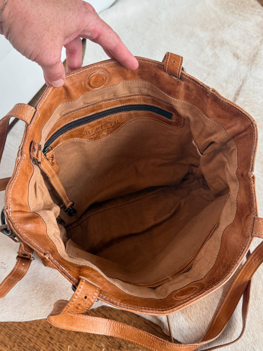 A hand holds open the Tahoka Leather Handbag by Savannah Sevens western life{&}style, showcasing its spacious interior lined with tan fabric and a zippered pocket along the back wall. This pecan dip dye crossbody combines elegance with practicality.