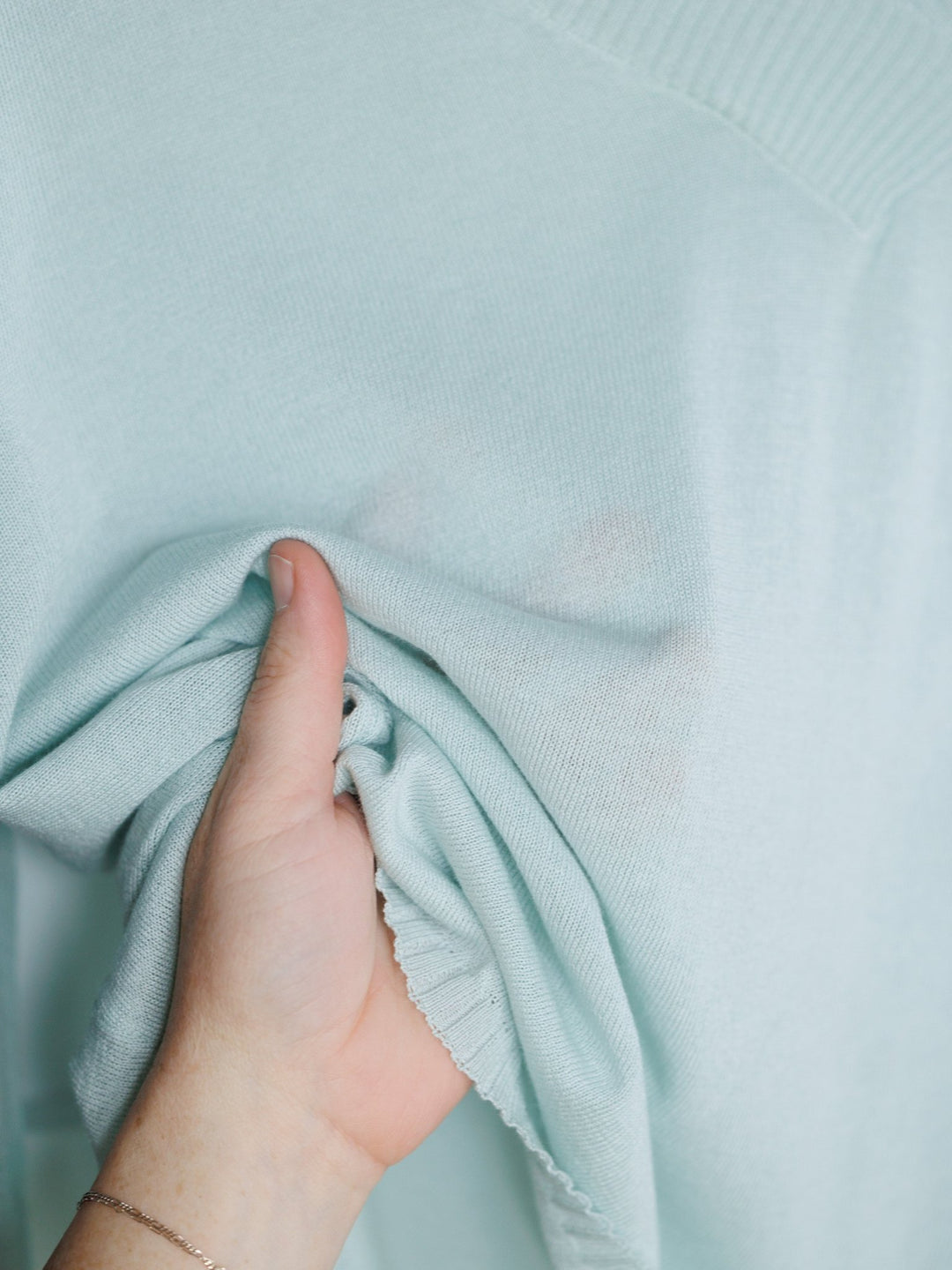 A hand gently pinches and lifts the soft, light seafoam fabric of the Tallula Light Seafoam Modal Top by Savannah Sevens western life{&}style, highlighting its relaxed fit and smooth texture.