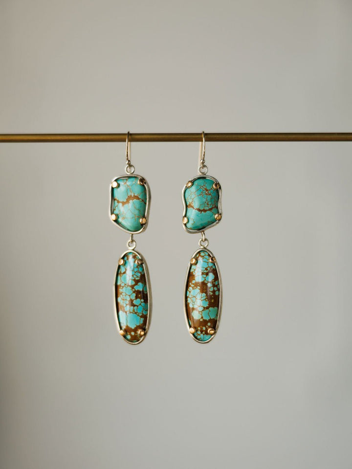 The Taos Earrings by Savannah Sevens western life{&}style feature Number 8 turquoise stones on top and elongated turquoise and brown oval drops set in gold, hanging from a horizontal rod.