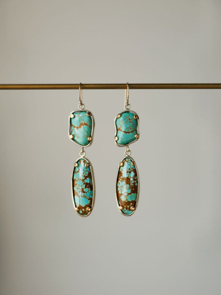 The Taos Earrings by Savannah Sevens western life{&}style feature Number 8 turquoise stones on top and elongated turquoise and brown oval drops set in gold, hanging from a horizontal rod.