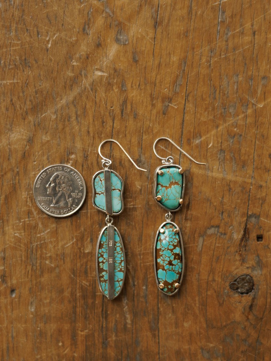 The Taos Earrings by Savannah Sevens western life{&}style, crafted in sterling silver with Number 8 turquoise stones and brown veining, are shown on wood beside a U.S. quarter to display their size.