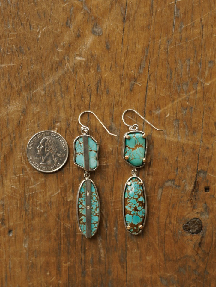 The Taos Earrings by Savannah Sevens western life{&}style, crafted in sterling silver with Number 8 turquoise stones and brown veining, are shown on wood beside a U.S. quarter to display their size.