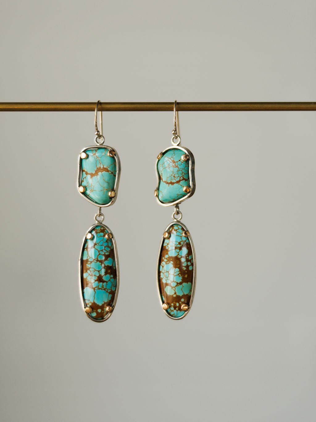 The Taos Earrings by Savannah Sevens western life{&}style feature sterling silver and irregular Number 8 turquoise stones with brown and gold matrix, set in silver frames and displayed against a plain background.
