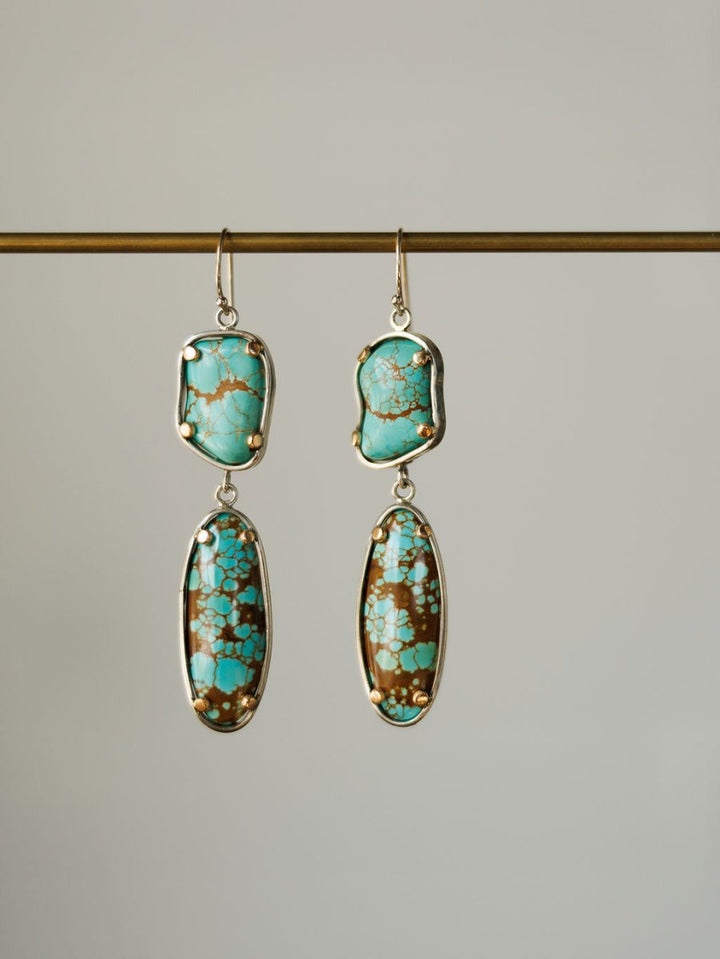 The Taos Earrings by Savannah Sevens western life{&}style feature sterling silver and irregular Number 8 turquoise stones with brown and gold matrix, set in silver frames and displayed against a plain background.