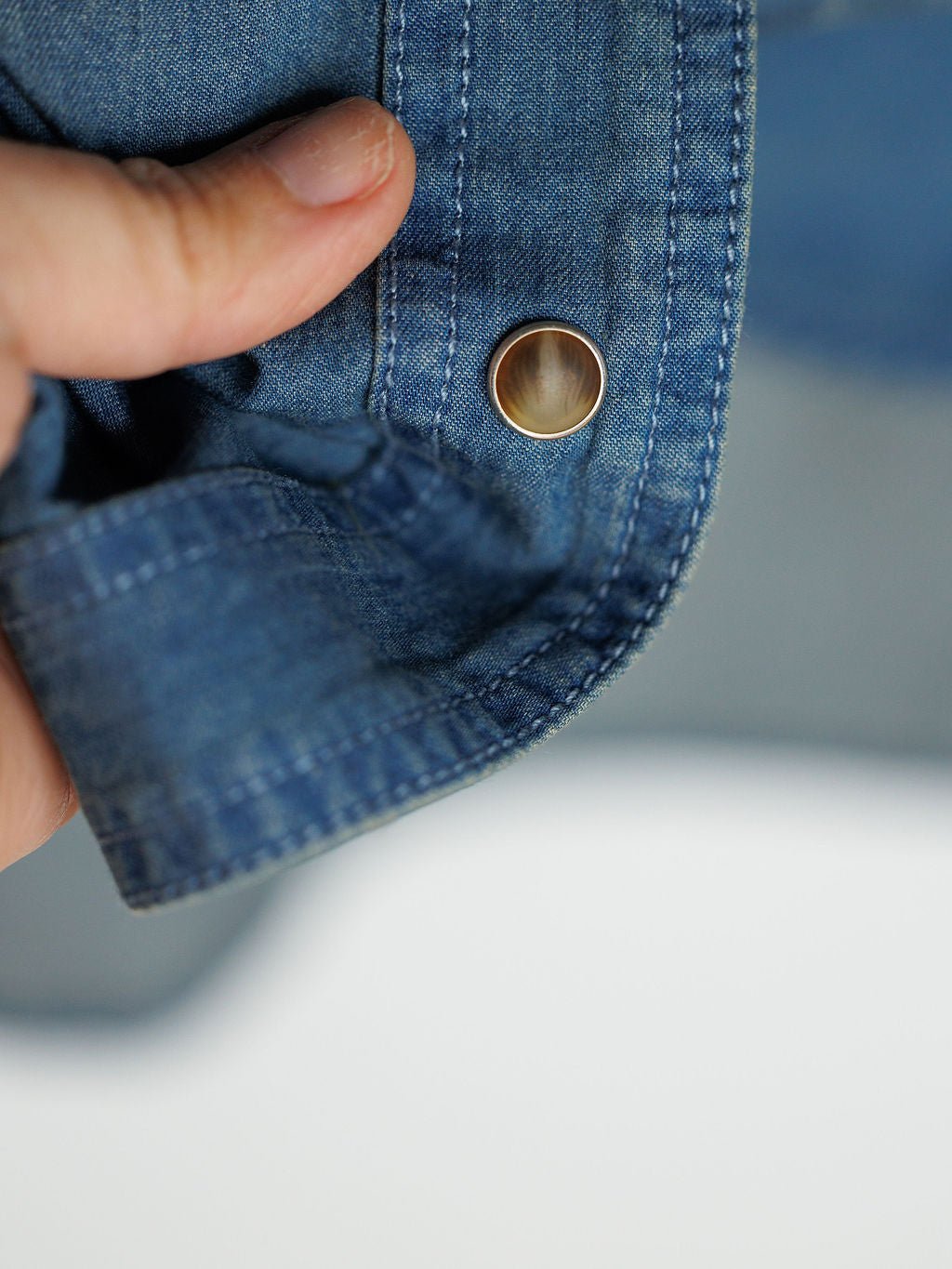 A close-up of a hand holding the cuff of the Savannah Sevens western life{&}style Tasha Rodeo Club Embroidered Denim Button Up, highlighting its metal snap button and detailed stitching.