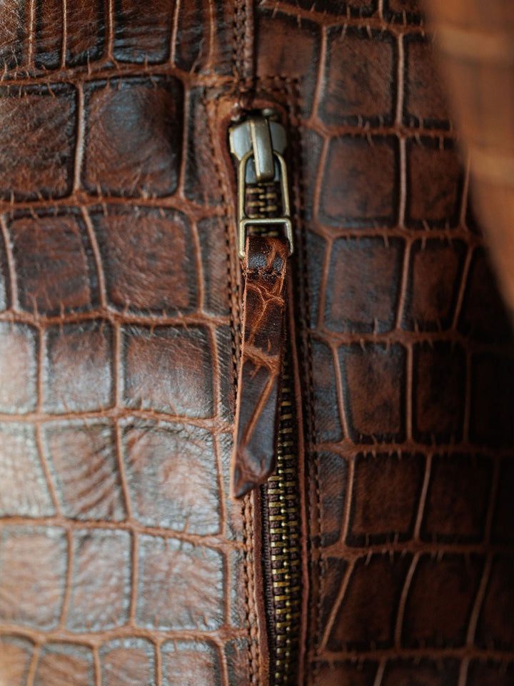 Close-up of The Tavares by Savannah Sevens western life{&}style, featuring rich brown crocodile-patterned leather and a brass zipper with a matching pull—ideal for fans of western or snip toe boot detailing. Boots by Ariat.