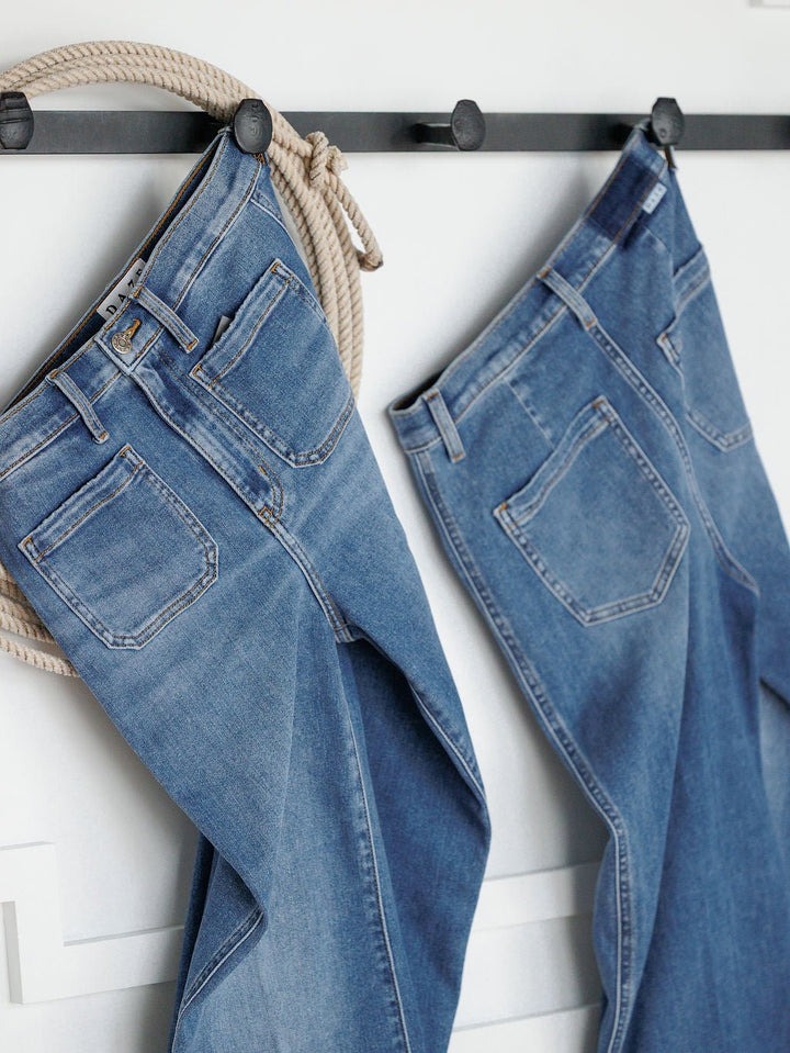 Two pairs of Savannah Sevens western life{&}style jeans hang side by side on black hooks against a white wall, including The Taylee High Rise Wide Leg Jean.