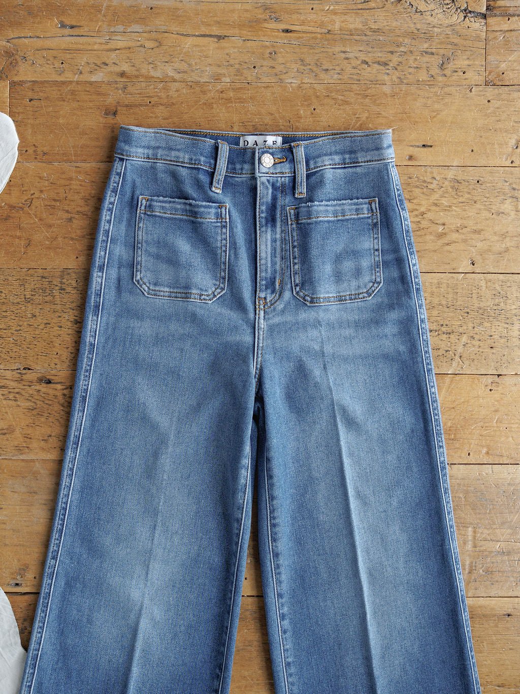 The Taylee High Rise Wide Leg Jean by Savannah Sevens western life{&}style in medium wash denim, featuring a high waist and front patch pockets, is laid flat on a wooden floor.