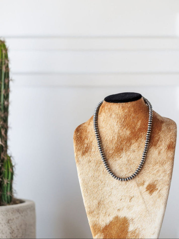 The Tecopa Necklace by Savannah Sevens western life{&}style is shown on a cowhide-covered display bust, with a green potted cactus to the left, all set against a white wall.