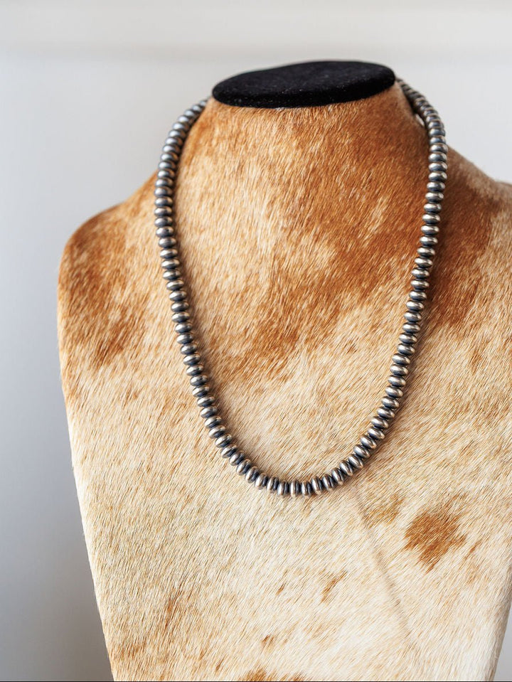 The Tecopa Necklace by Savannah Sevens western life{&}style, a sterling silver Navajo pearl design, is displayed on a brown and white cowhide-patterned jewelry bust against a light background.