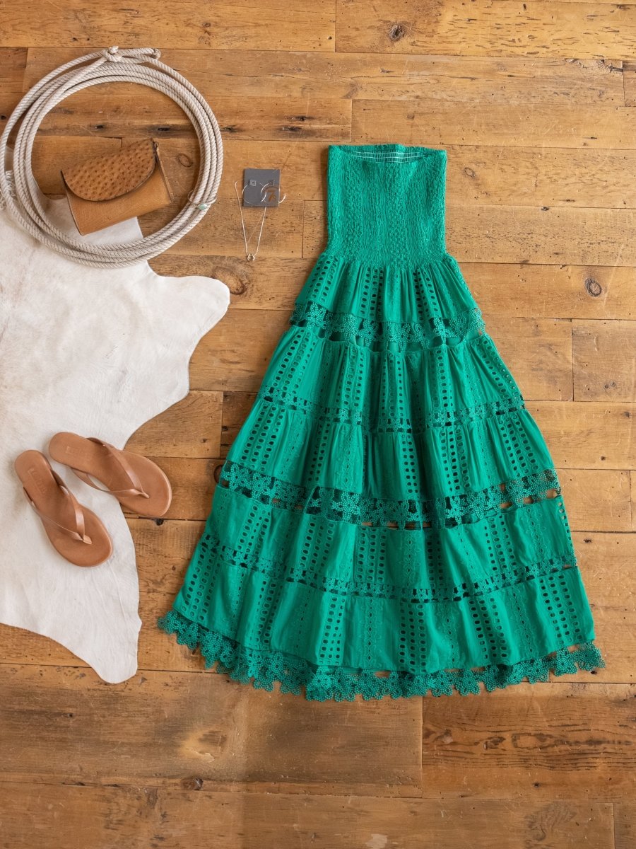 The Tekoa Jade Teal Crochet Strapless Dress by Savannah Sevens western life{&}style is styled on a wooden floor with tan sandals, a white round purse, a brown textured clutch, a silver necklace, and a white cowhide rug.