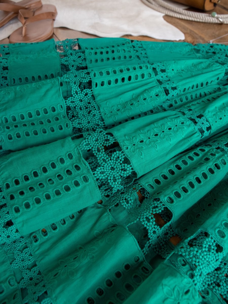 A close-up of the Tekoa Jade Teal Crochet Strapless Dress by Savannah Sevens western life{&}style, featuring eyelet patterns and crochet lace, laid flat with tan sandals and a white accessory in the background.