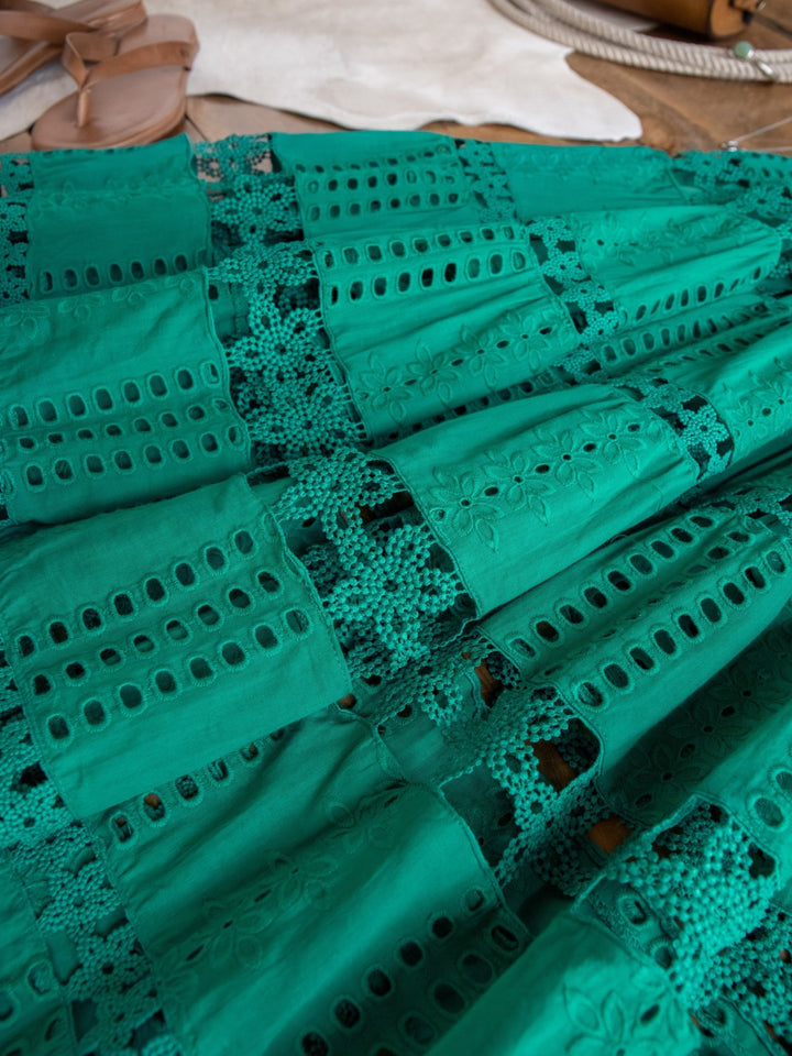 A close-up of the Tekoa Jade Teal Crochet Strapless Dress by Savannah Sevens western life{&}style, featuring eyelet patterns and crochet lace, laid flat with tan sandals and a white accessory in the background.
