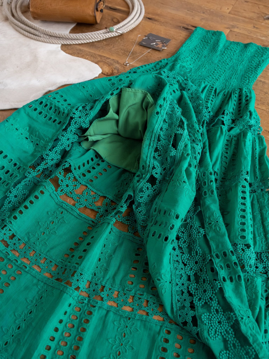 The Tekoa Jade Teal Crochet Strapless Dress by Savannah Sevens western life{&}style is displayed on a wooden floor with a white rug and necklace in the background.