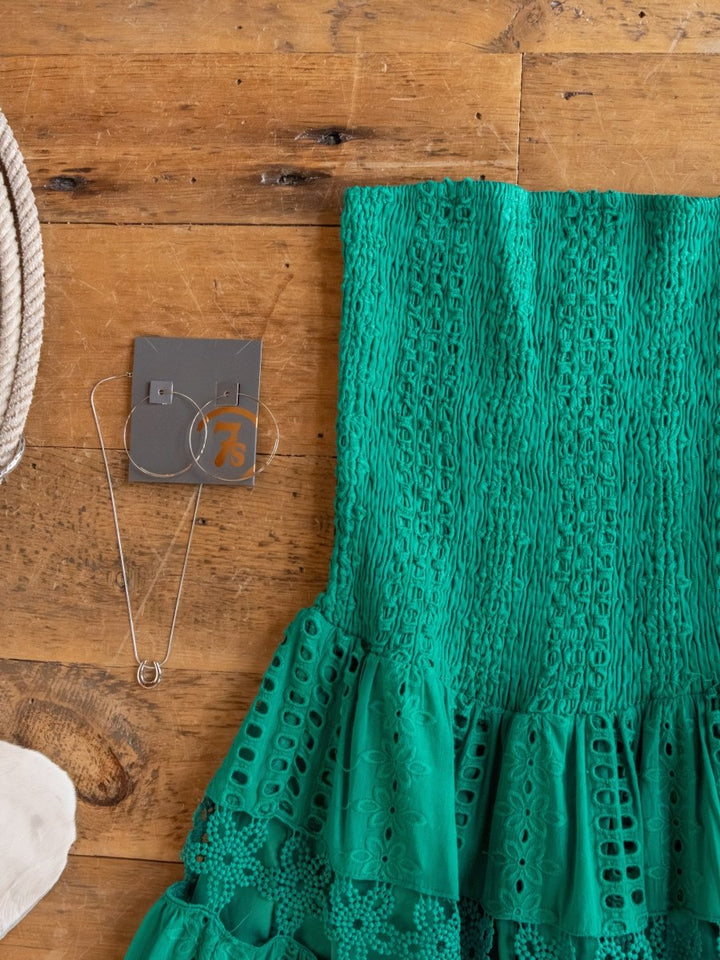 The Tekoa Jade Teal Crochet Strapless Dress by Savannah Sevens western life{&}style is shown on a wooden surface with a silver necklace, hoop earrings on a gray card, and nearby coiled rope.