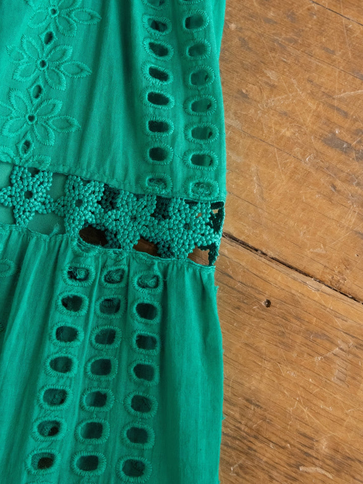 A close-up of the Tekoa Jade Teal Crochet Strapless Dress by Savannah Sevens western life{&}style shows green fabric with intricate cut-out patterns and floral embroidery, combining solid and openwork sections for a decorative textured effect.