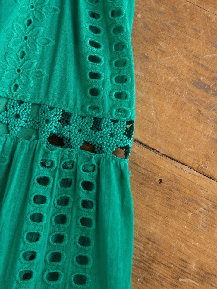 A close-up of the Tekoa Jade Teal Crochet Strapless Dress by Savannah Sevens western life{&}style shows green fabric with intricate cut-out patterns and floral embroidery, combining solid and openwork sections for a decorative textured effect.