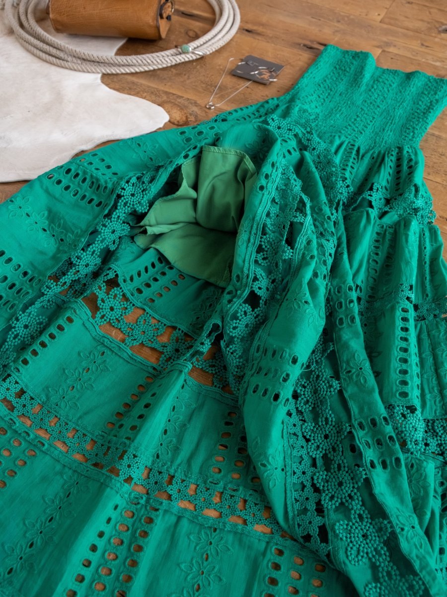 The Tekoa Jade Teal Crochet Strapless Dress by Savannah Sevens western life{&}style is displayed on a wooden floor with a white rug and necklace in the background.