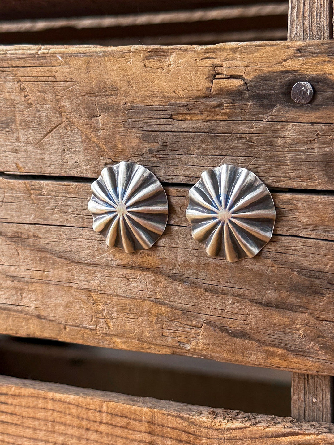 Two Tempe Sterling Silver Parachute Earrings by Savannah Sevens western life{&}style are displayed on rustic, weathered wooden planks, highlighting their shiny, textured surface and raised, radiating scalloped pattern.