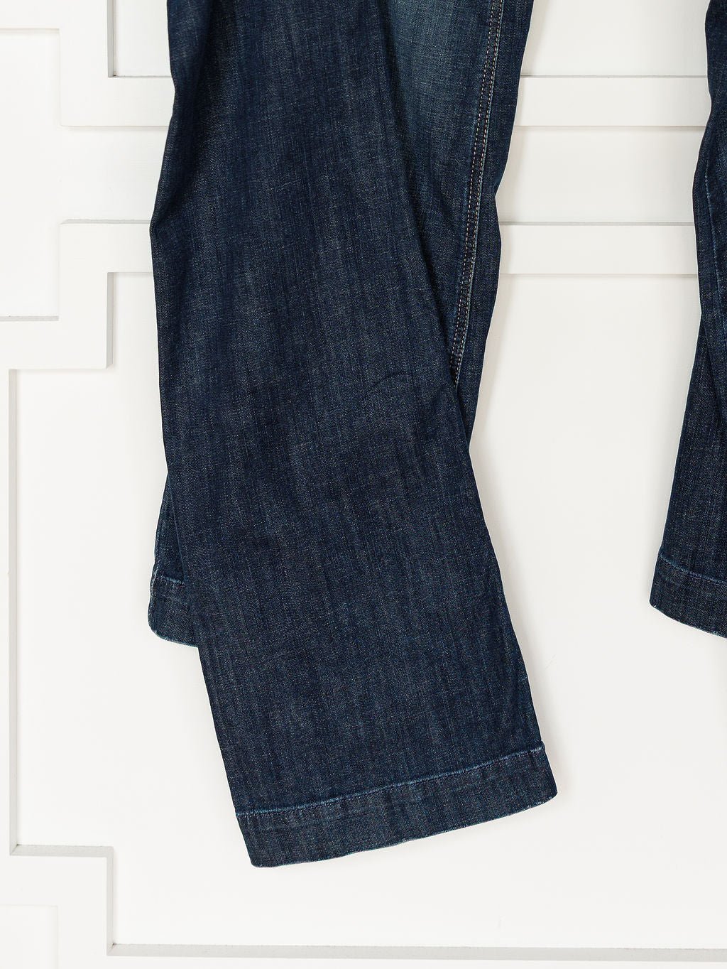 A close-up of Ariat's The Tex Perfect Rise Trouser Jean in medium dark wash denim, highlighting the wide leg and hem against a white background with decorative paneling.