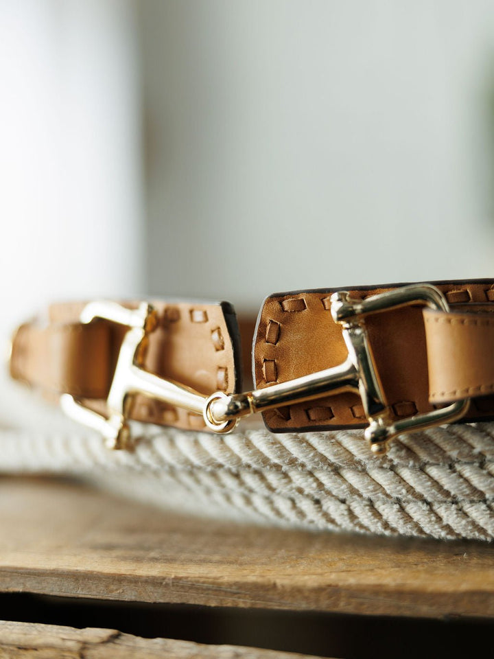 Close-up of the Texarkana Belt by Savannah Sevens western life{&}style, featuring saddle tan leather, detailed stitching, and shiny gold hardware, displayed on a coiled rope atop a wooden surface.