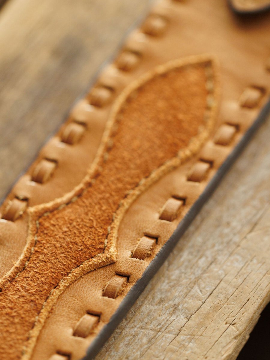 Close-up of the Texarkana Belt by Savannah Sevens western life{&}style, featuring saddle tan leather with stitched and embossed patterns. The belt’s detailed craftsmanship is highlighted by its visible texture and neat stitching on wood.