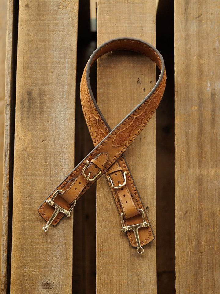 The Texarkana Belt by Savannah Sevens western life{&}style, in saddle tan leather with decorative stitching and metal buckles, is displayed crossed on a wooden pallet background.