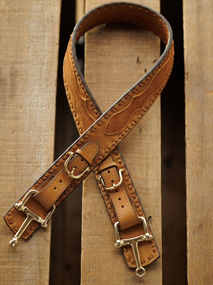 Two Savannah Sevens western life{&}style Texarkana Belts in saddle tan leather with brass buckles and engraved patterns are crossed on a wooden surface.