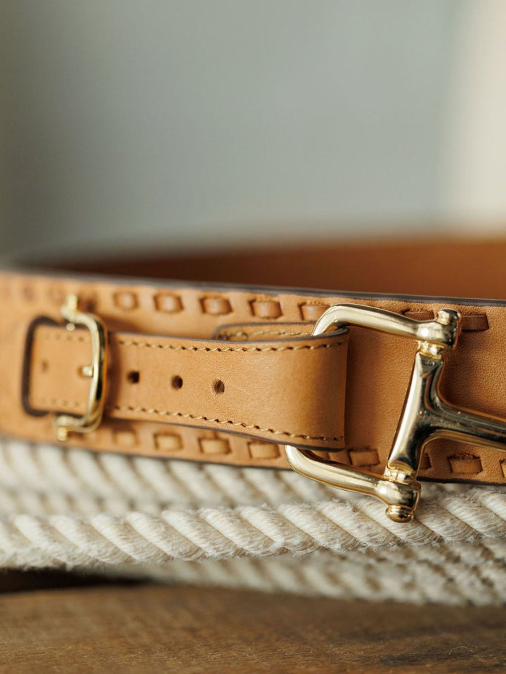 Close-up of the Texarkana Belt by Savannah Sevens western life{&}style, featuring light brown leather with decorative stitching and a shiny gold buckle, displayed on a coiled white rope.