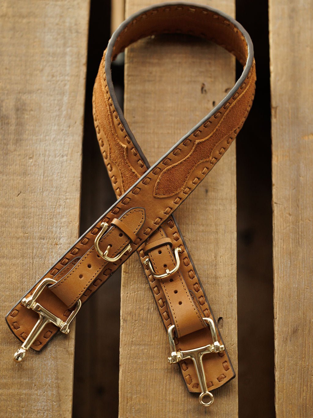 Two Savannah Sevens western life{&}style Texarkana Belts in saddle tan leather with brass buckles and engraved patterns are crossed on a wooden surface.
