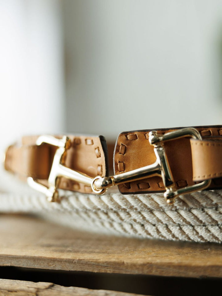 Close-up of the Texarkana Belt by Savannah Sevens western life{&}style, featuring saddle tan leather, detailed stitching, and shiny gold hardware, displayed on a coiled rope atop a wooden surface.
