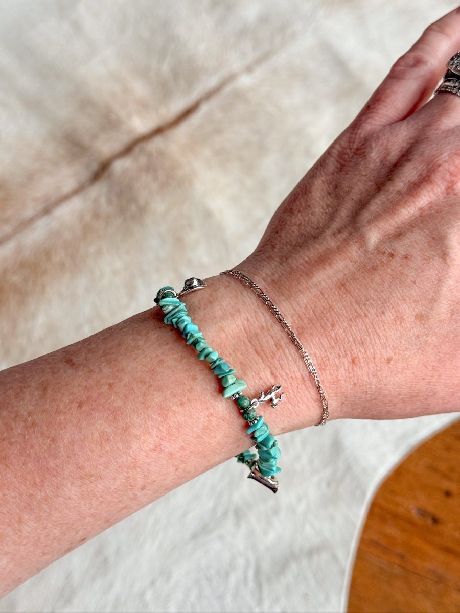 A wrist wearing the Savannah Sevens western life{&}style Texas City Bracelet, a sterling silver chain with turquoise and small silver charms, set against a soft, light-colored background.