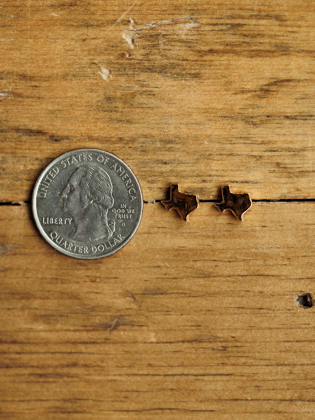 A U.S. quarter and the Texas Earrings by Savannah Sevens western life{&}style are displayed on a wooden surface.