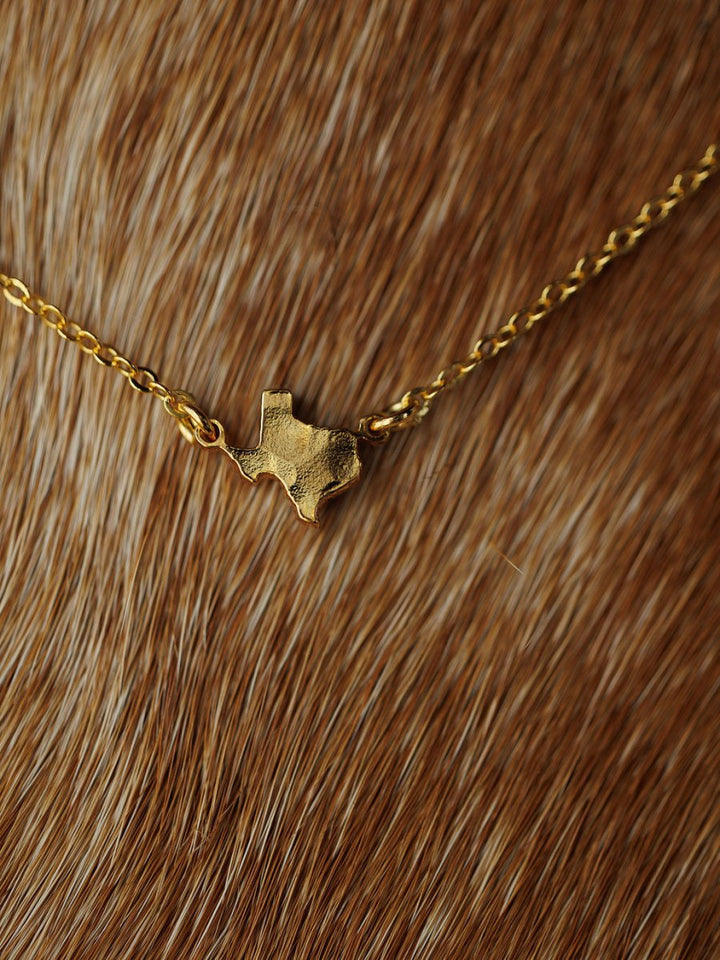 The Savannah Sevens western life{&}style Texas Necklace, featuring a state-shaped pendant, is displayed on a brown and white fur background.