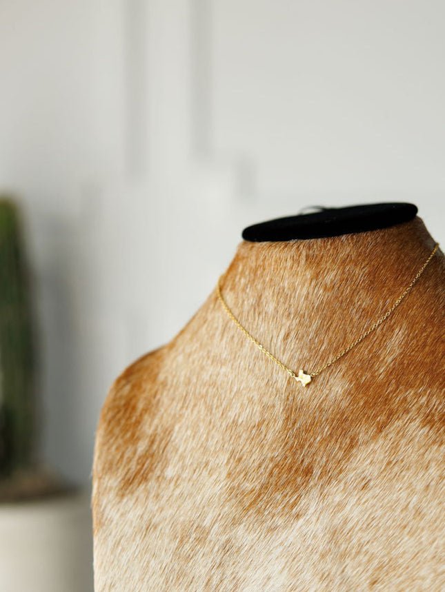 The Savannah Sevens western life{&}style Texas Necklace, featuring a delicate gold Texas pendant, is shown on a tan and white fur-covered bust with a softly blurred light background.