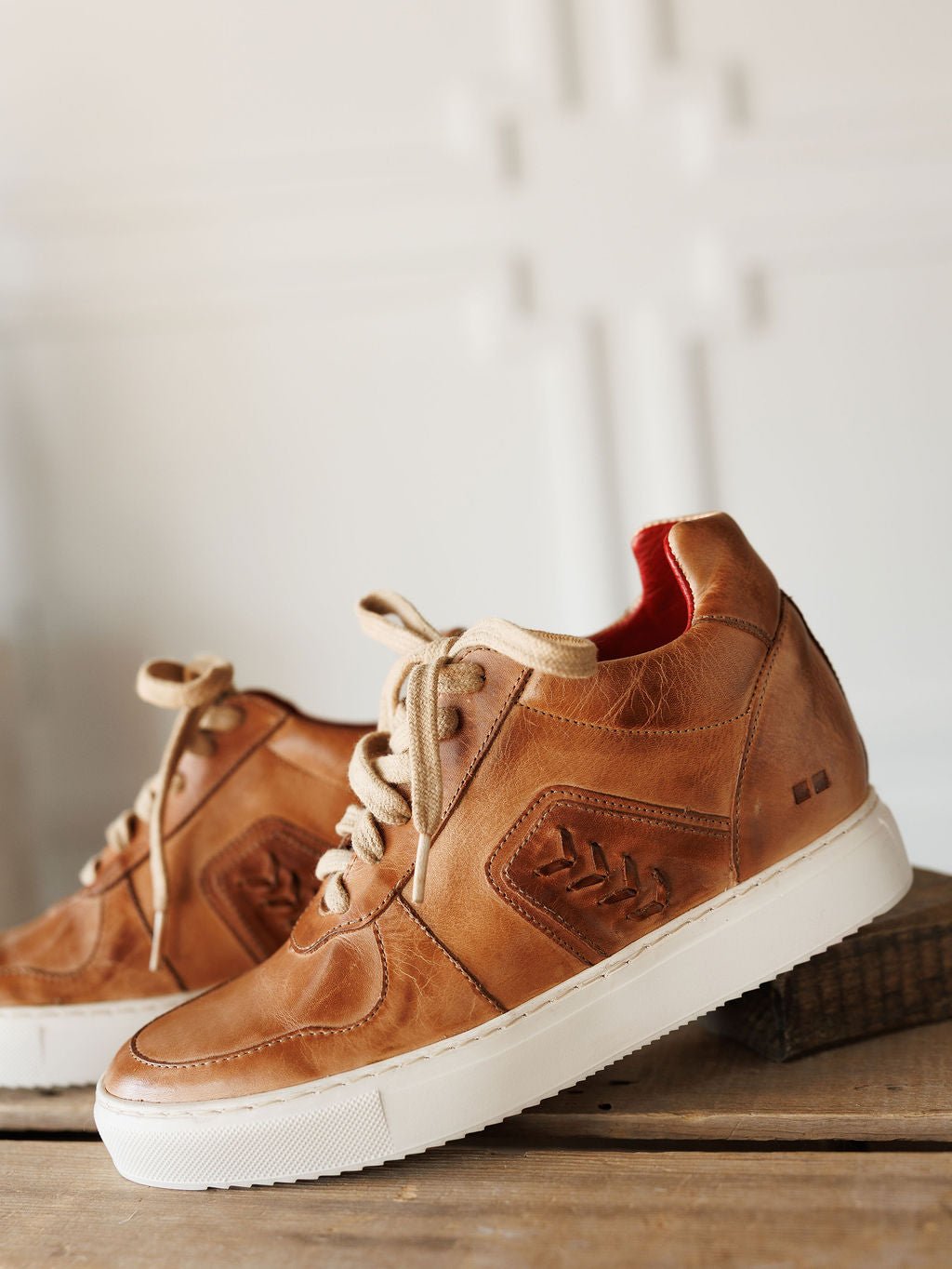 The Texicos by Savannah Sevens western life{&}style: tan leather sneakers with beige laces and white soles, displayed on wood with a neutral background. One shoe is raised on a small wooden block. Made by BedStu. 
