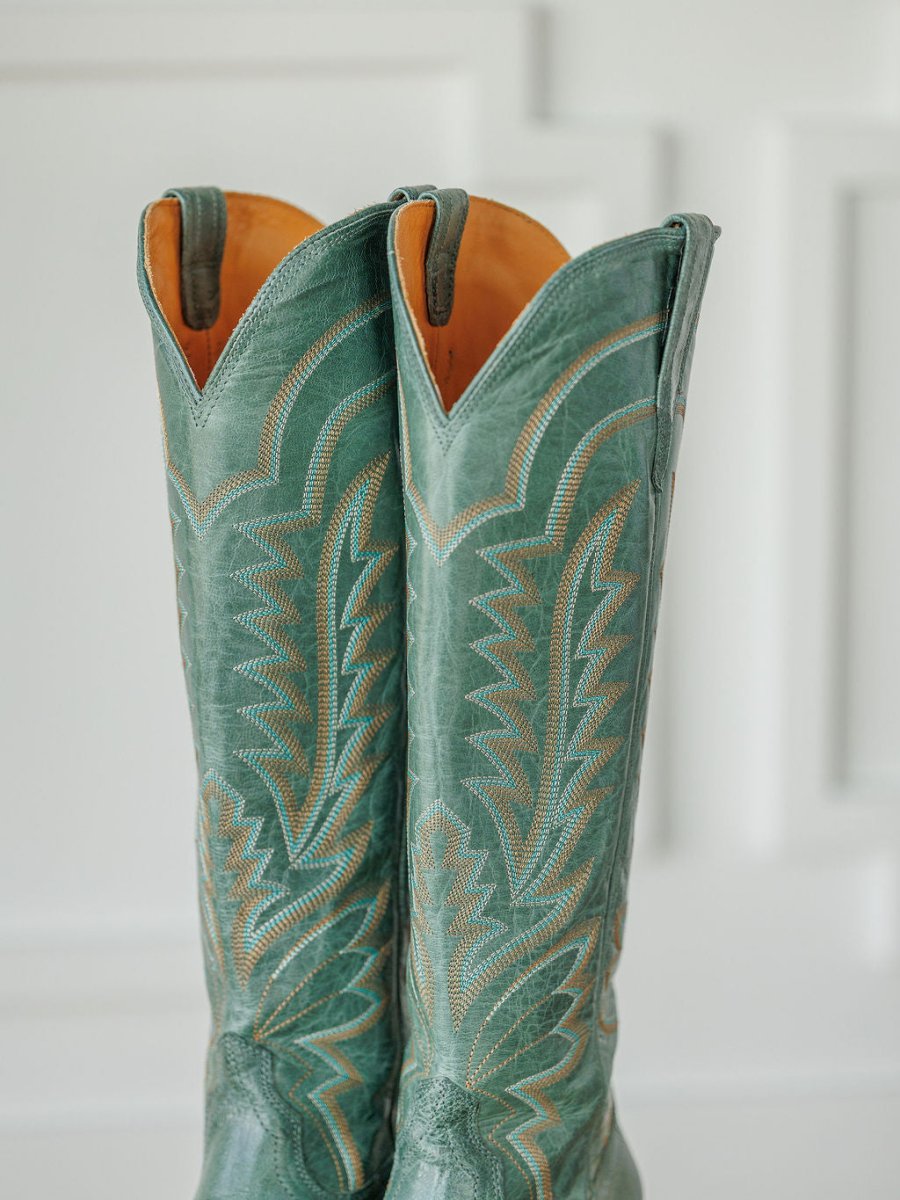 Two tall, green The Abby Boot {Sagebrush} by Savannah Sevens western life{&}style stand side by side, featuring tan stitching, decorative patterns, pull straps, and a pointed top against a white background. Boots handmade by Tecovas.
