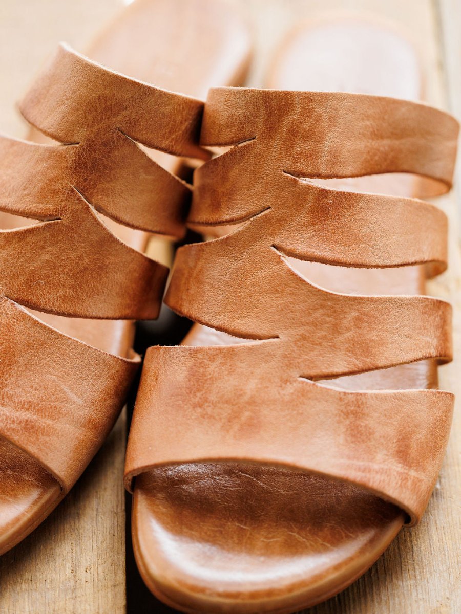 Close-up of The Acomas sandal by Savannah Sevens western life{&}style, featuring multiple wavy tan leather straps, displayed on a wooden surface. Sandals made by BedStu.