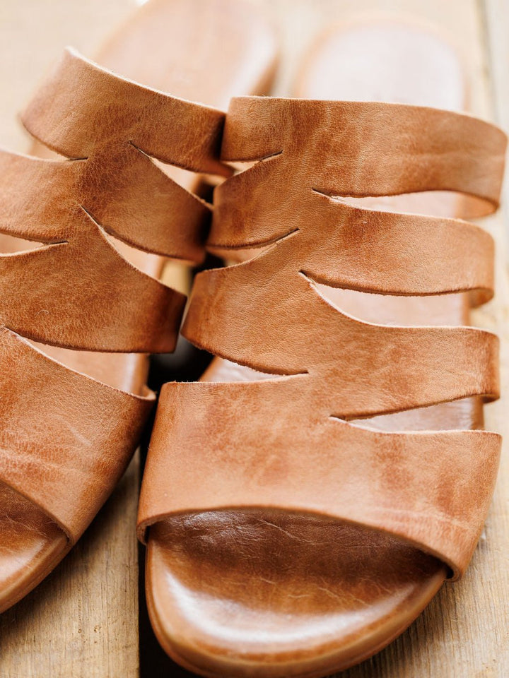 Close-up of The Acomas sandal by Savannah Sevens western life{&}style, featuring multiple wavy tan leather straps, displayed on a wooden surface. Sandals made by BedStu.