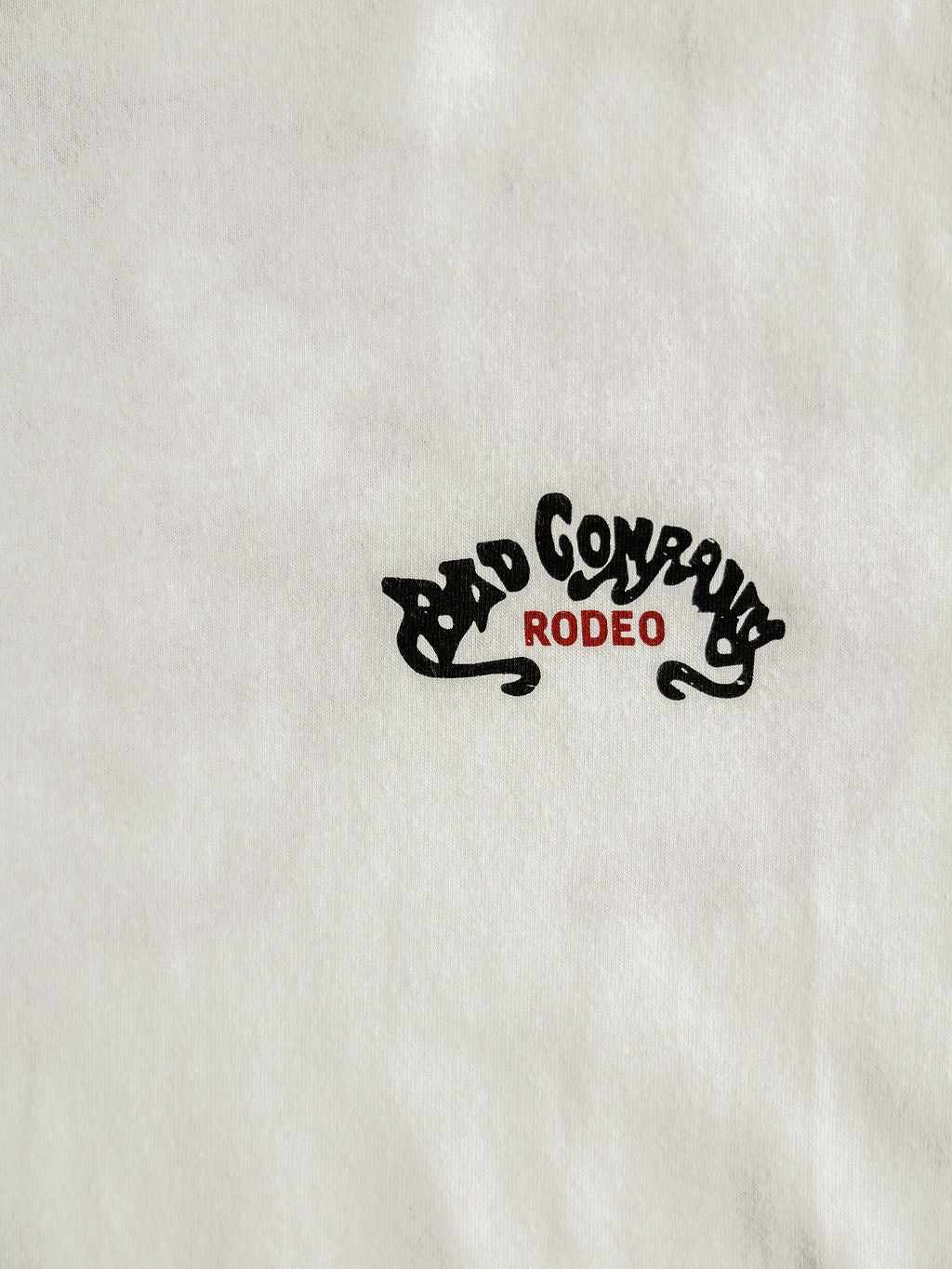 The Bad Company Men's Graphic Tee by Savannah Sevens western life{&}style is a white men's shirt with bold black "BAD COMPANY" above red "RODEO," blending classic style with the Bad Company Rodeo vibe.