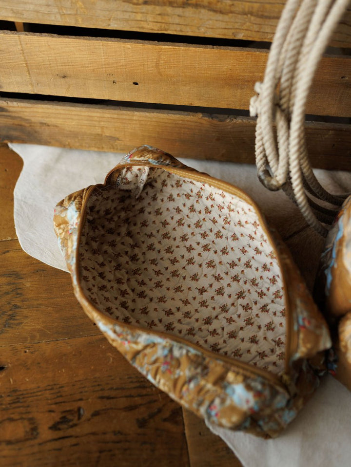 An open quilted bag from the Big Sky Collection by Savannah Sevens western life&style, lined with a floral pattern, rests on a wooden surface beside rope and a wooden crate.