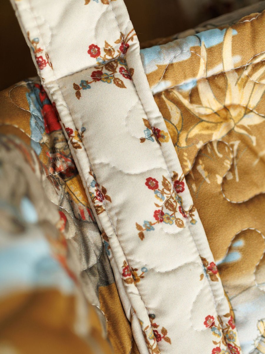Close-up of a quilted bag set from The Big Sky Collection by Savannah Sevens western life&style, featuring small red flowers and green leaves on a cream background with gold and blue accents.