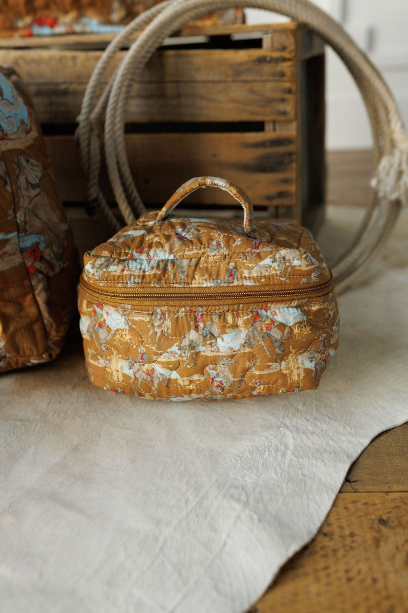 A small quilted fabric bag from The Big Sky Collection by Savannah Sevens western life&style, featuring a vintage cowboy print, sits on a white rug beside a wooden crate and coiled rope on a wooden floor.