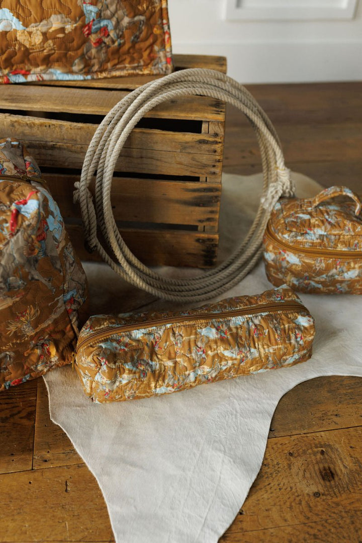 The Big Sky Collection by Savannah Sevens western life&style features textured brown and blue patterned travel bags displayed on a white hide rug next to a coiled rope and wooden crate atop a rustic wooden floor.