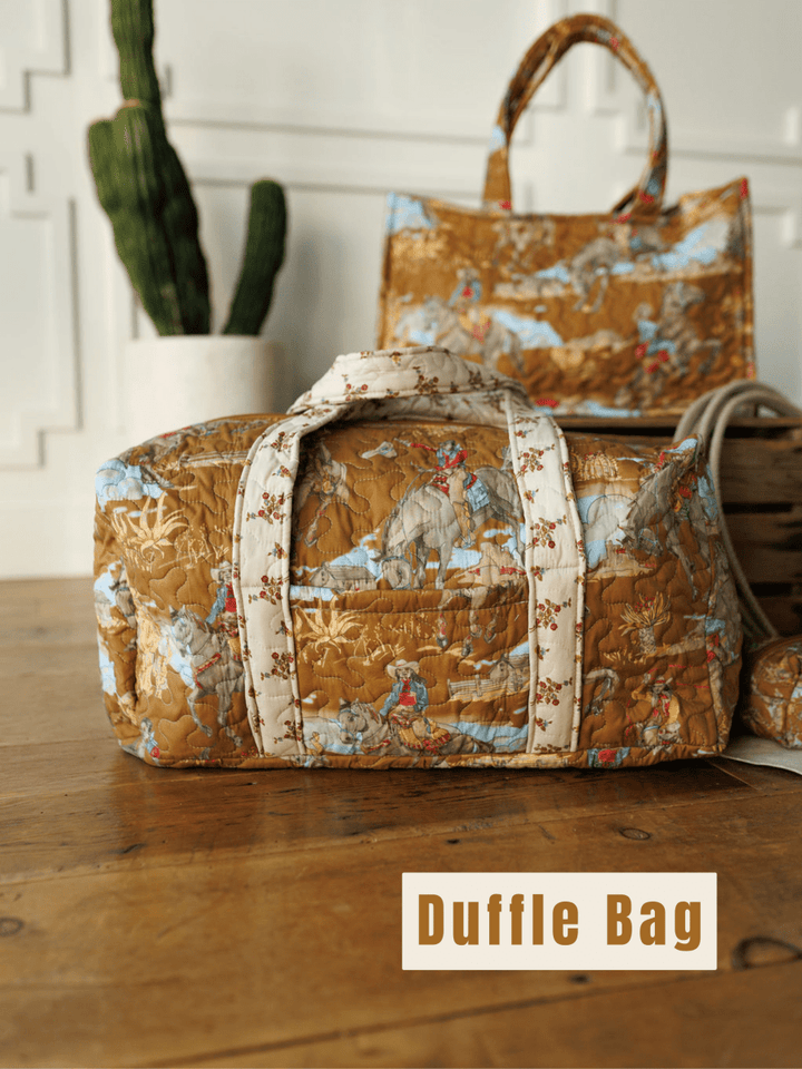 A brown quilted duffle bag from The Big Sky Collection by Savannah Sevens western life&style rests on a wooden floor. Matching tote and basket are behind it, near a potted cactus. “Duffle Bag” is shown in bold text.