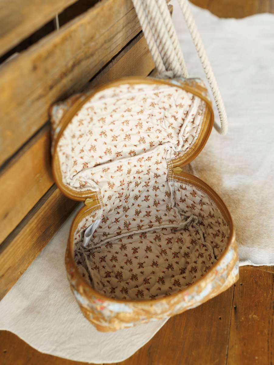 Open, oval-shaped bag from the Big Sky Collection by Savannah Sevens western life&style, featuring a floral fabric lining and a textured, vintage-look exterior. Shown on a white rug beside wooden crates.