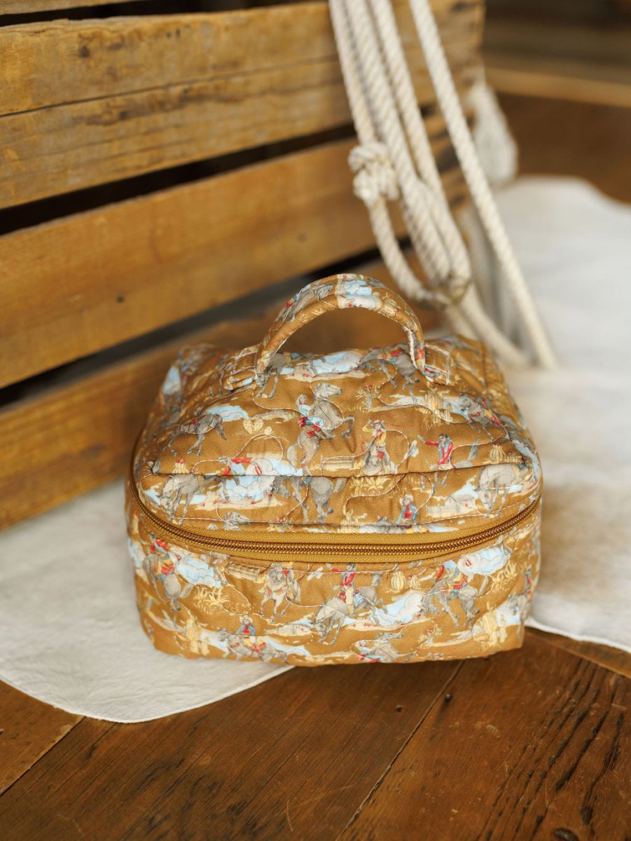 A quilted, square floral travel bag from The Big Sky Collection by Savannah Sevens western life&style sits on a light rug near coiled rope and wooden crates atop a wooden floor.