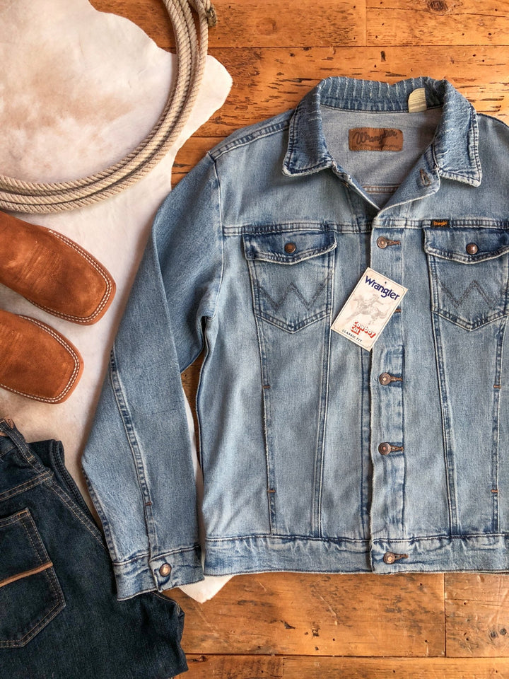 A light blue Savannah Sevens western life&style The Boden {Men's} jacket with tags is laid on a wooden floor beside brown leather boots, dark jeans, and a white animal hide rug.