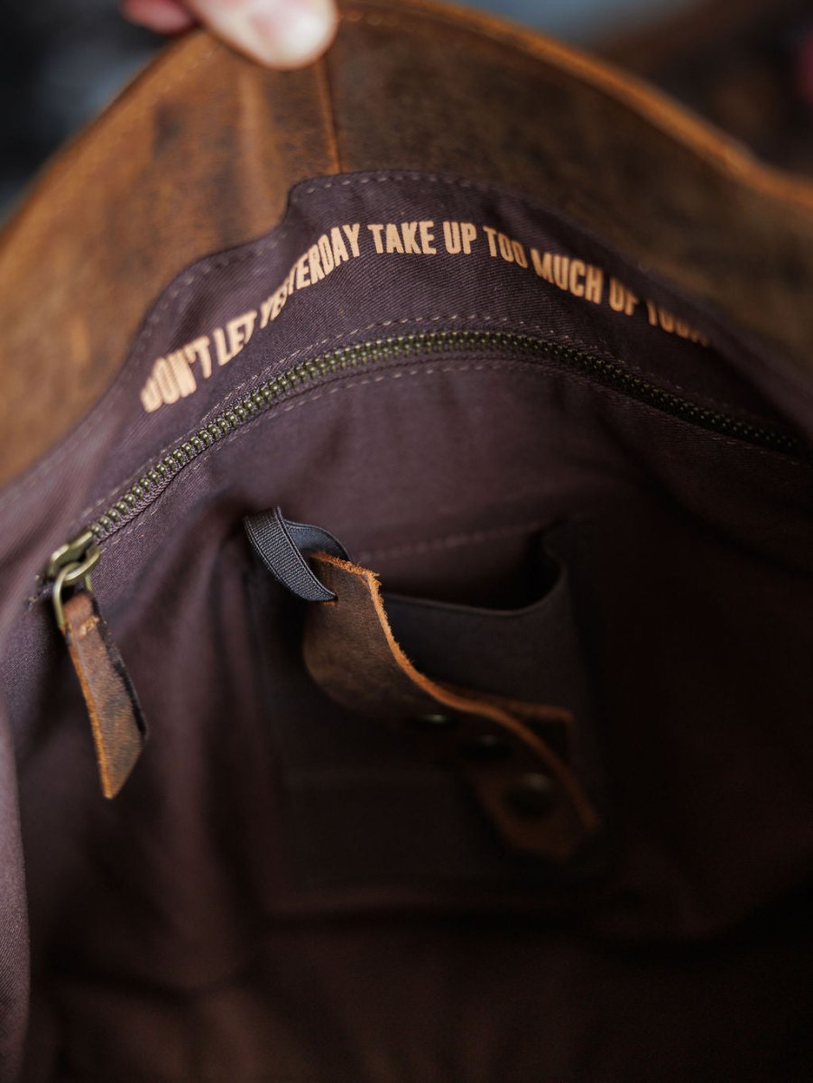 Close-up of the inside of The Broken Arrow genuine leather handbag by Savannah Sevens western life{&}style, featuring a zipper with “Don’t let yesterday take up too much of today” and an interior leather key strap.