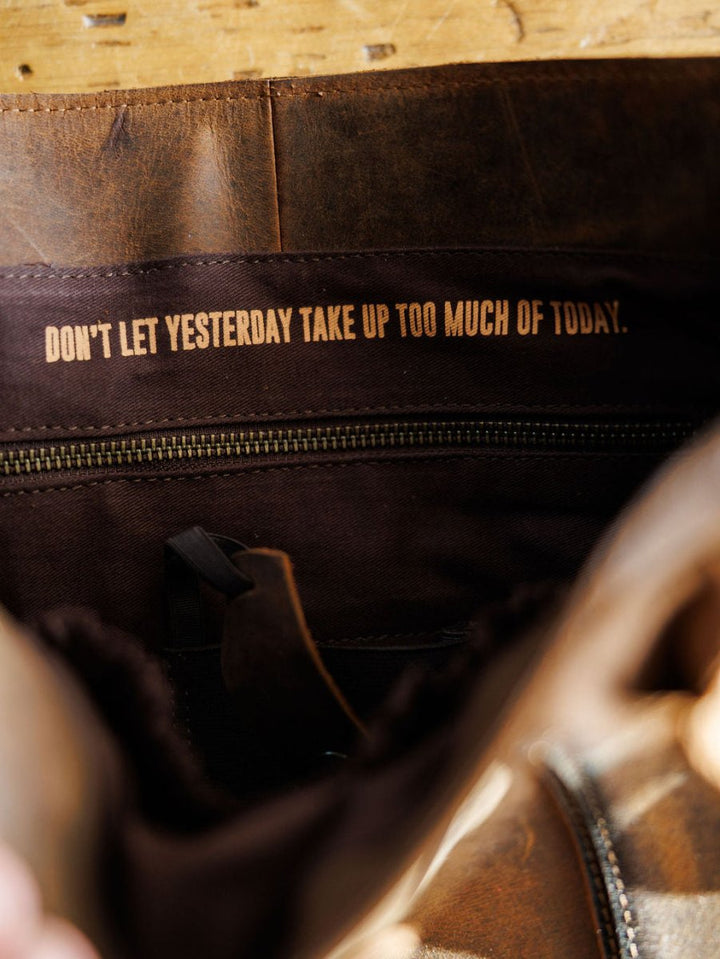 A close-up of the inside of The Broken Arrow handbag by Savannah Sevens western life{&}style shows "DONT LET YESTERDAY TAKE UP TOO MUCH OF TODAY." printed above a zippered pocket.